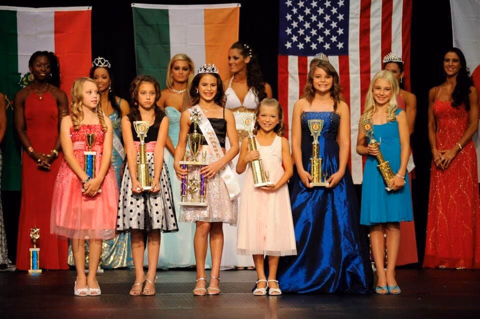 Stage is filled with junior competitors holding their trophies and smiling