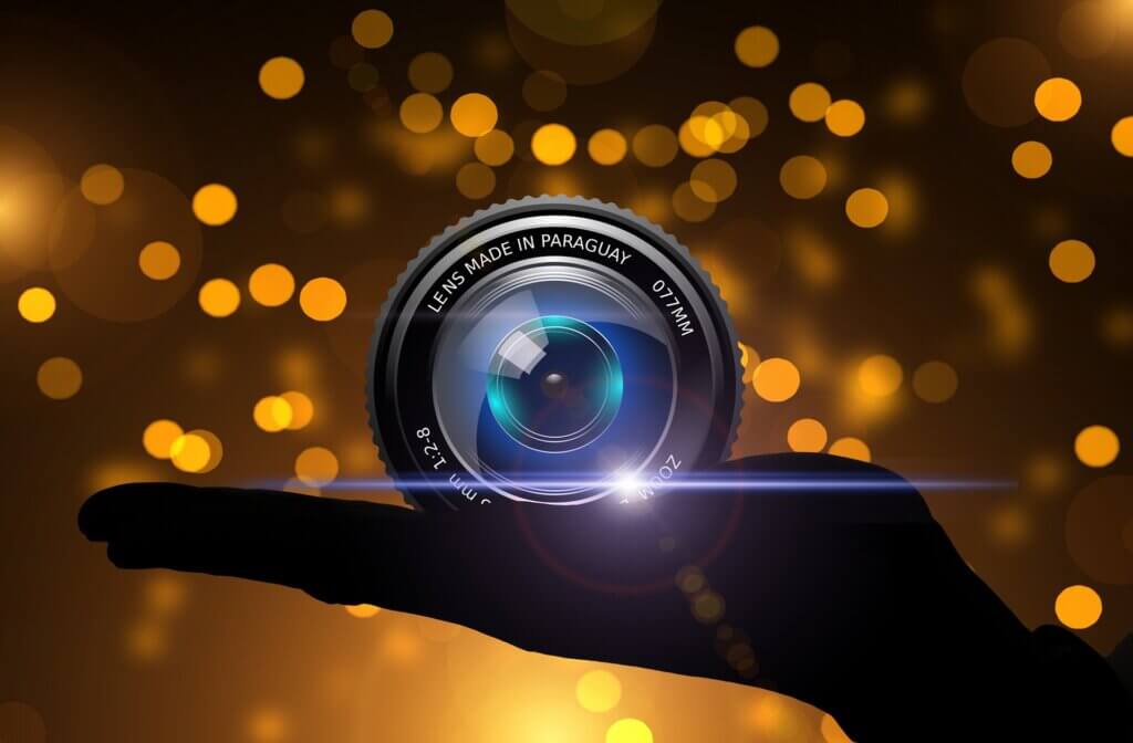 A hand holding a camera lens against a shimmering gold background